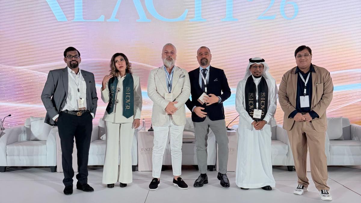 Group photo of six conference participants on stage at REACH 2026 in Saudi Arabia.